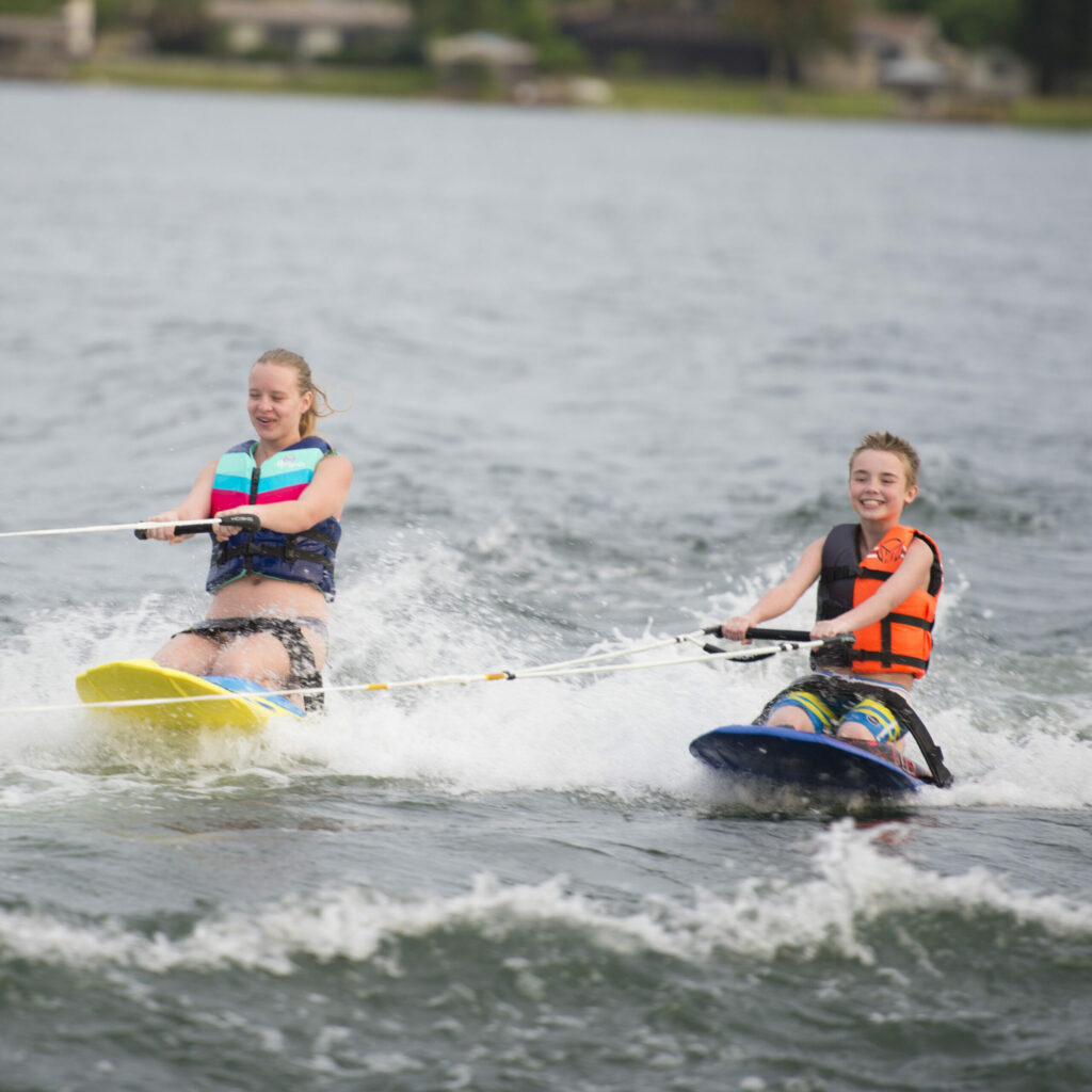 A boy and a girl on kneeboards riding across a lake.