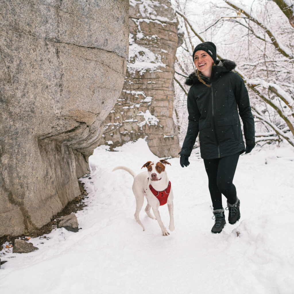 A woman and her dog walking through snow covered terrain on a winter hiking trip.