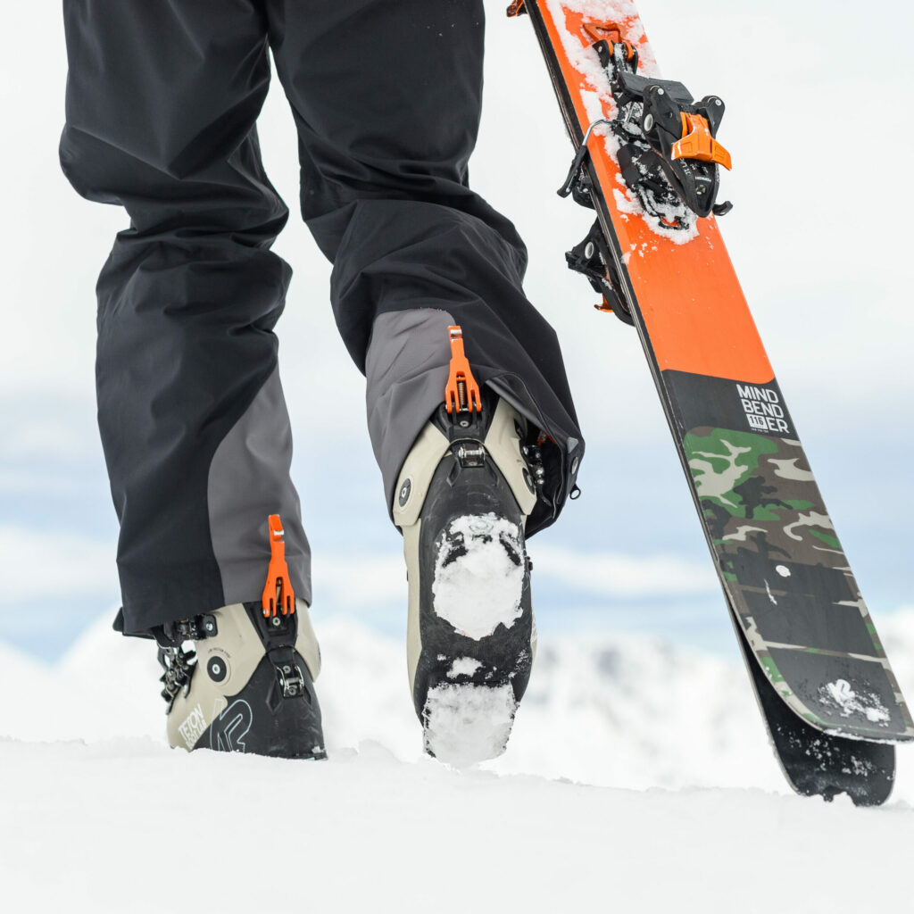 A man carrying skis through the snow in ski boots.