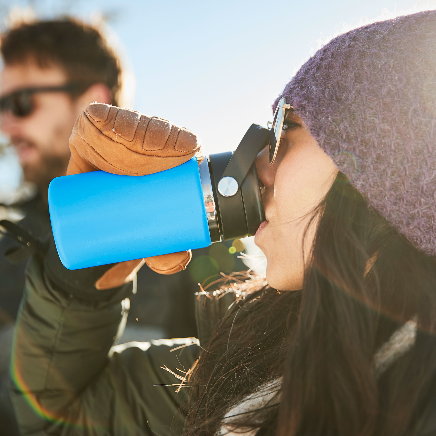 A woman drinking out of a blue insulated cup.