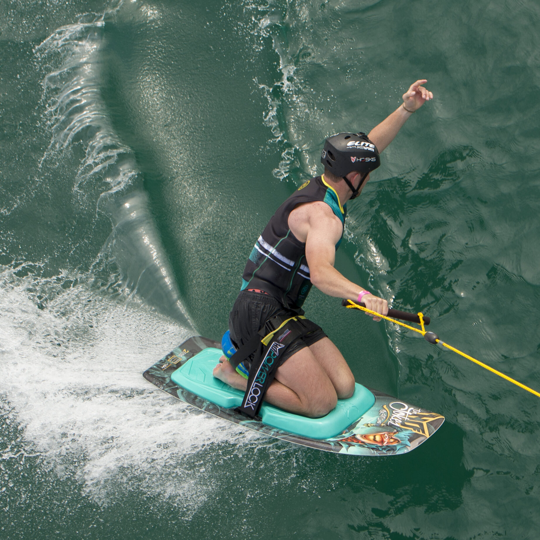A man signaling to the boat as he makes a turn on an HO Sports kneeboard.
