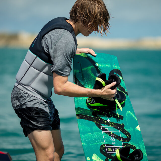 A man adjusting his boots on a wakeboard.