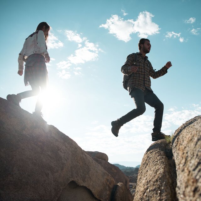 A man and woman walking over some boulders, geared up with Keen Hiking Boots.