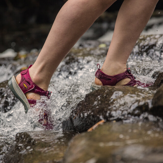 A woman walking up a streambed with Keen Sandals.