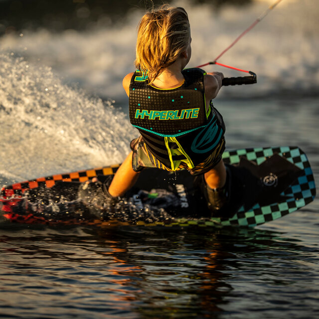 A kid carving a wake while the sun sets on a Hyperlite Wakeboard.