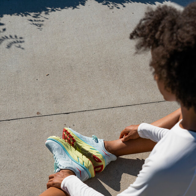 A woman resting on a sidewalk after a run with Hoka One Running Shoes.