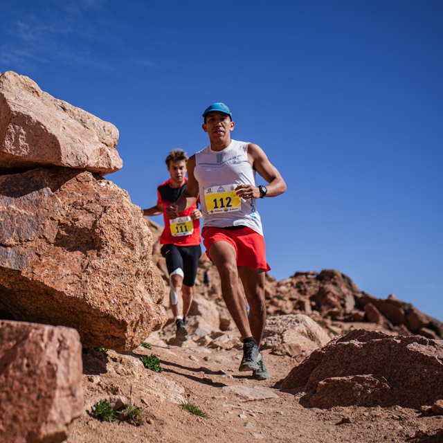 Runners in a race coming down a steep decline on a rocky trail.
