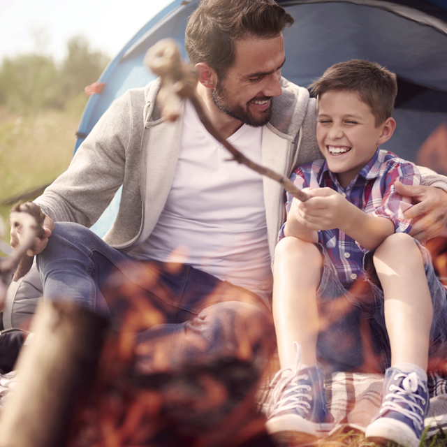 A father and son roasting marshmallows at the campsite.