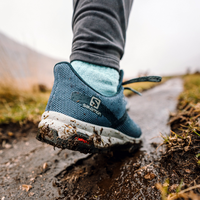 A runner with blue Solomon shoes on a muddy trail.