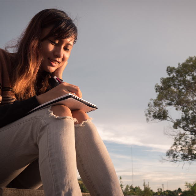 A woman sitting down and sketching in a sketchbook.