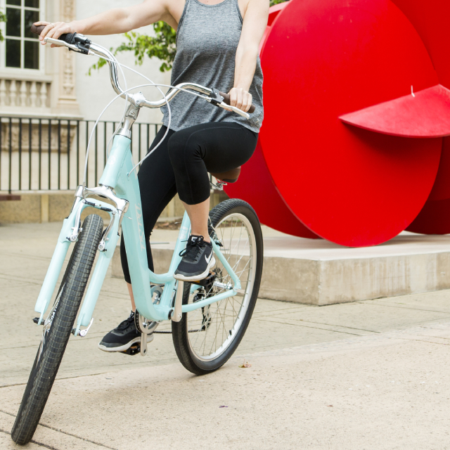 Woman riding bike by an abstract red sculpture.