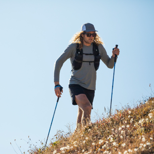 Man hiking up a steep hill with trekking poles.