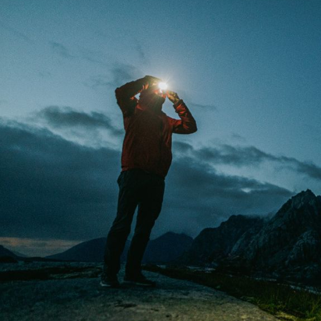 Person in extreme hiking gear with a headlamp shining brightly in dim light.