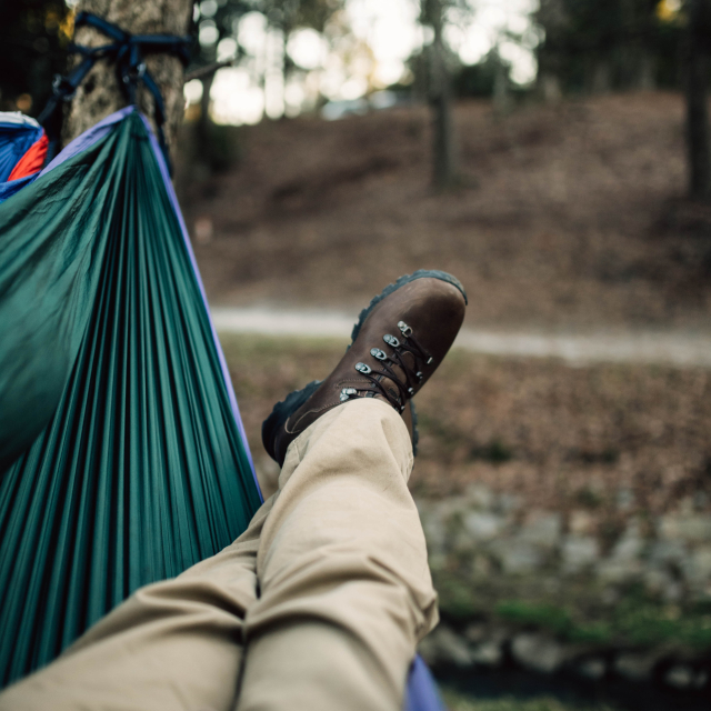 A person in hiking boots lying in a synthetic hammock.