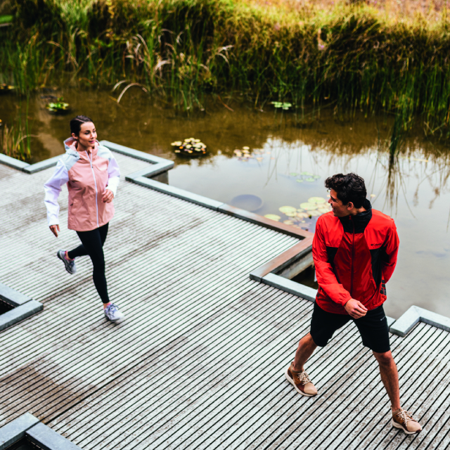 Two people walking on a bridge over a pond.