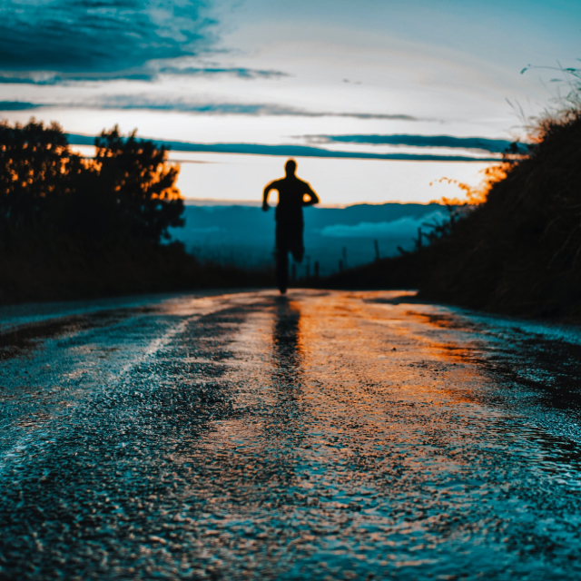 Light from dusk reflecting off wet pavement with the silhouette of a person running.