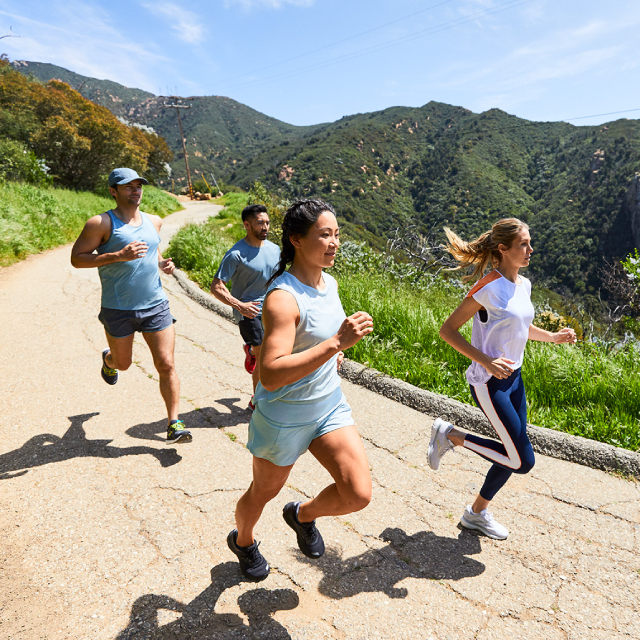 Group of four running along a small road surrounded by forested hills.