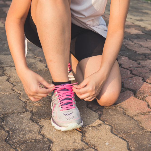 Woman kneeling to tie running shoes with neon pink shoelaces.