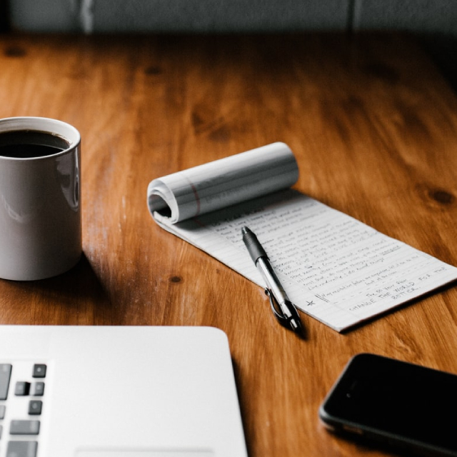 Notepad, computer, and coffee on a wooden table.