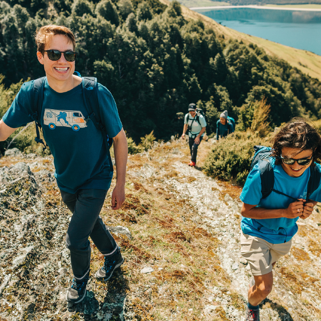 Grinning hikers walking up a hill from a lake.