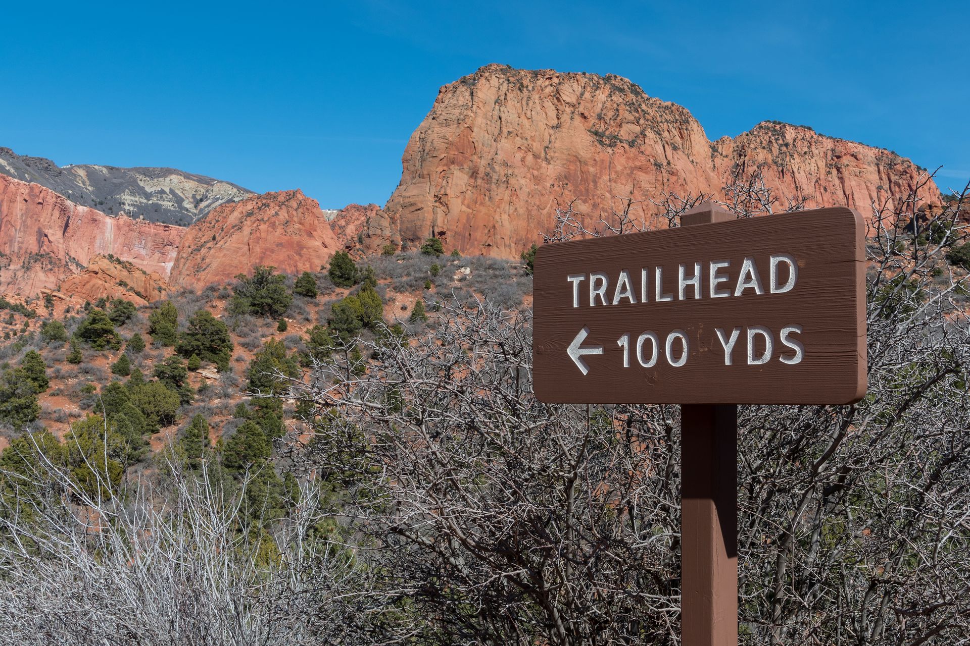 Sign reading “Trailhead, 100 yards” with an arrow pointing towards a rocky incline.