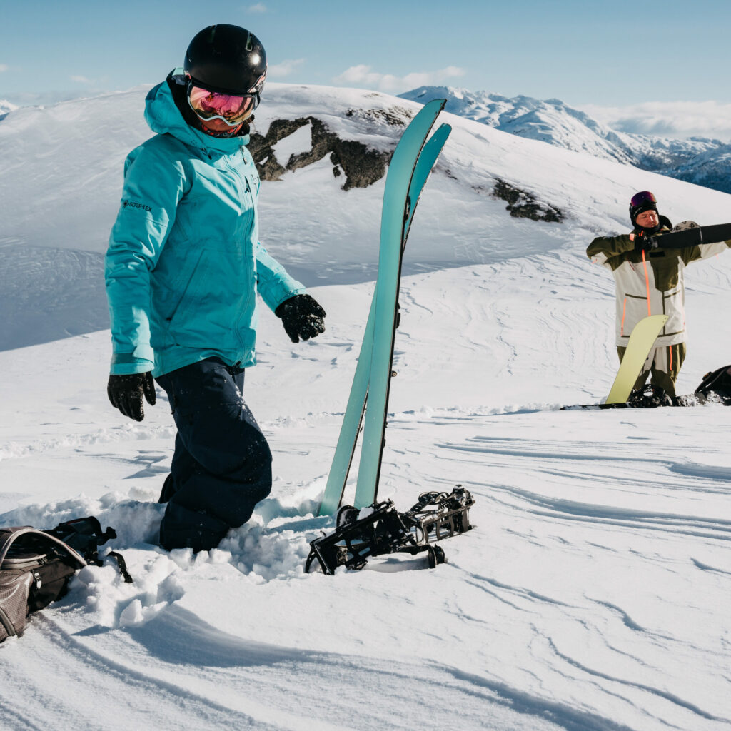 A skier and snowboarder getting ready in some packed snow.