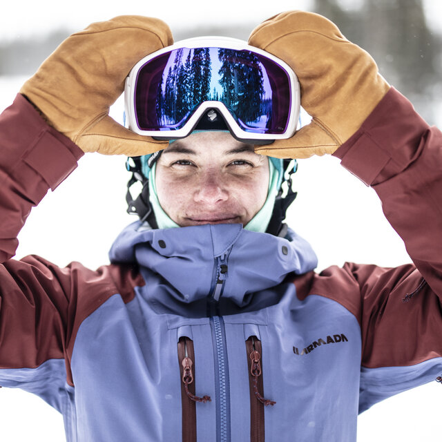 A woman putting on a pair of goggles over her helmet.