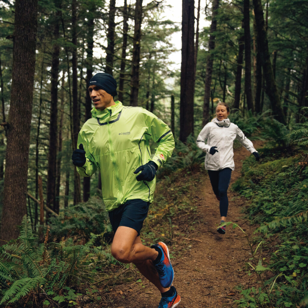 Two people running on a trail in the woods.
