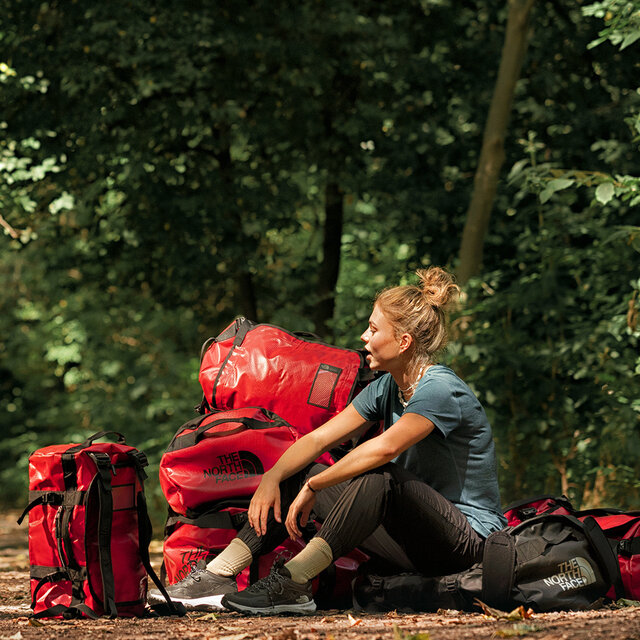 A woman sitting among a pile of red The North Face duffel bags.