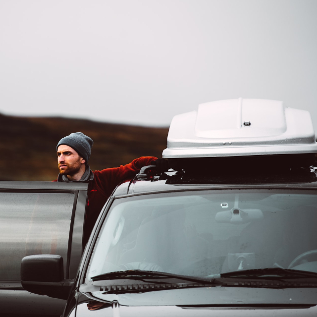 A man exits his car, looking out over rocky and cold environment.