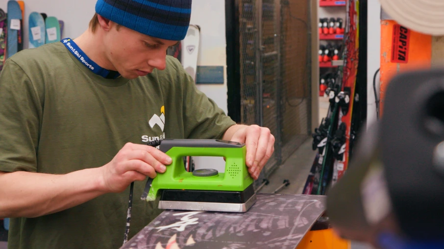 Outdoor expert hand waxing snowboard at Sun & Ski Sports